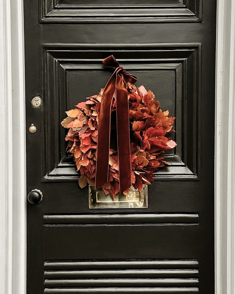 Autumn wreath with red leaves and a brown ribbon on a black door.