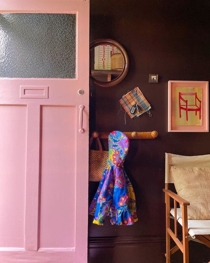 Pink door with colorful raincoat, mirror, and framed picture on a dark wall.