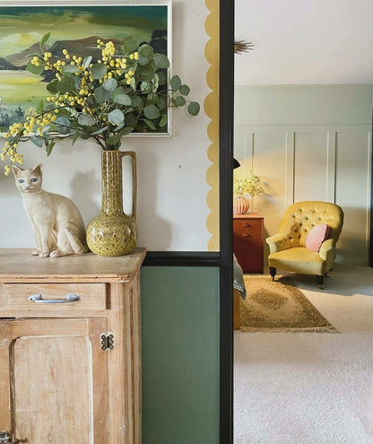 Room interior with a vase of flowers, cat statue, and yellow armchair.