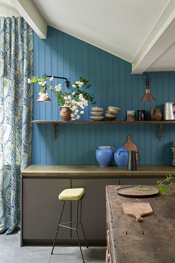 Kitchen interior with blue walls, wooden shelves, and a bar stool.