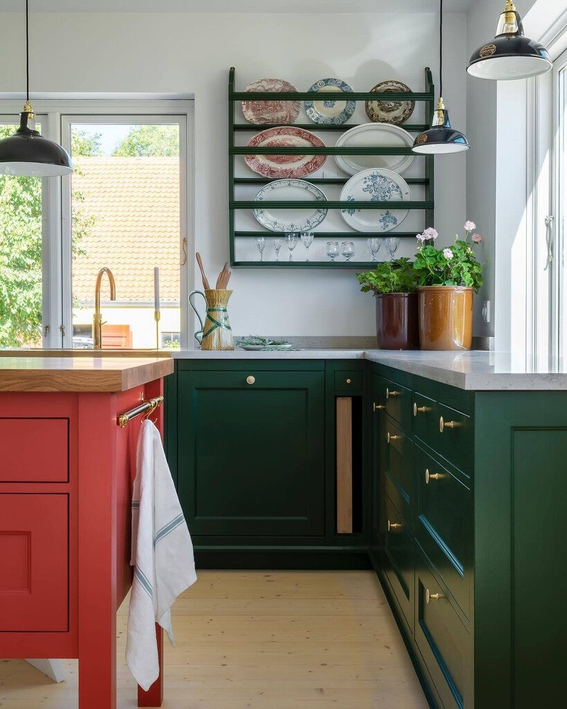 Modern kitchen with green cabinets, red island, and decorative plates on a wall shelf.