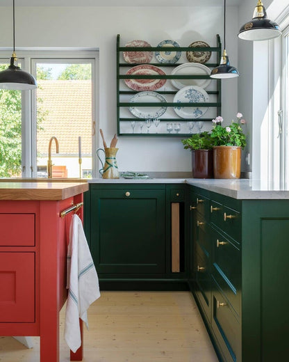 Modern kitchen with green cabinets, red island, and decorative plates on a wall shelf.