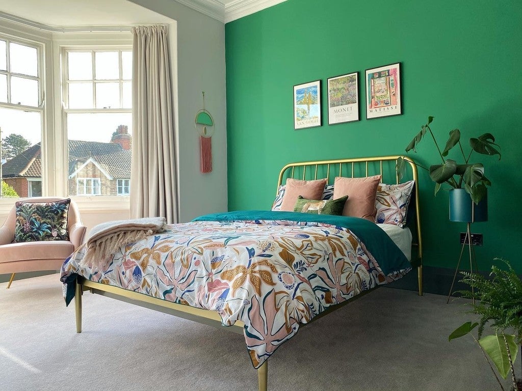 Bedroom with green wall, gold bed frame, and floral bedding