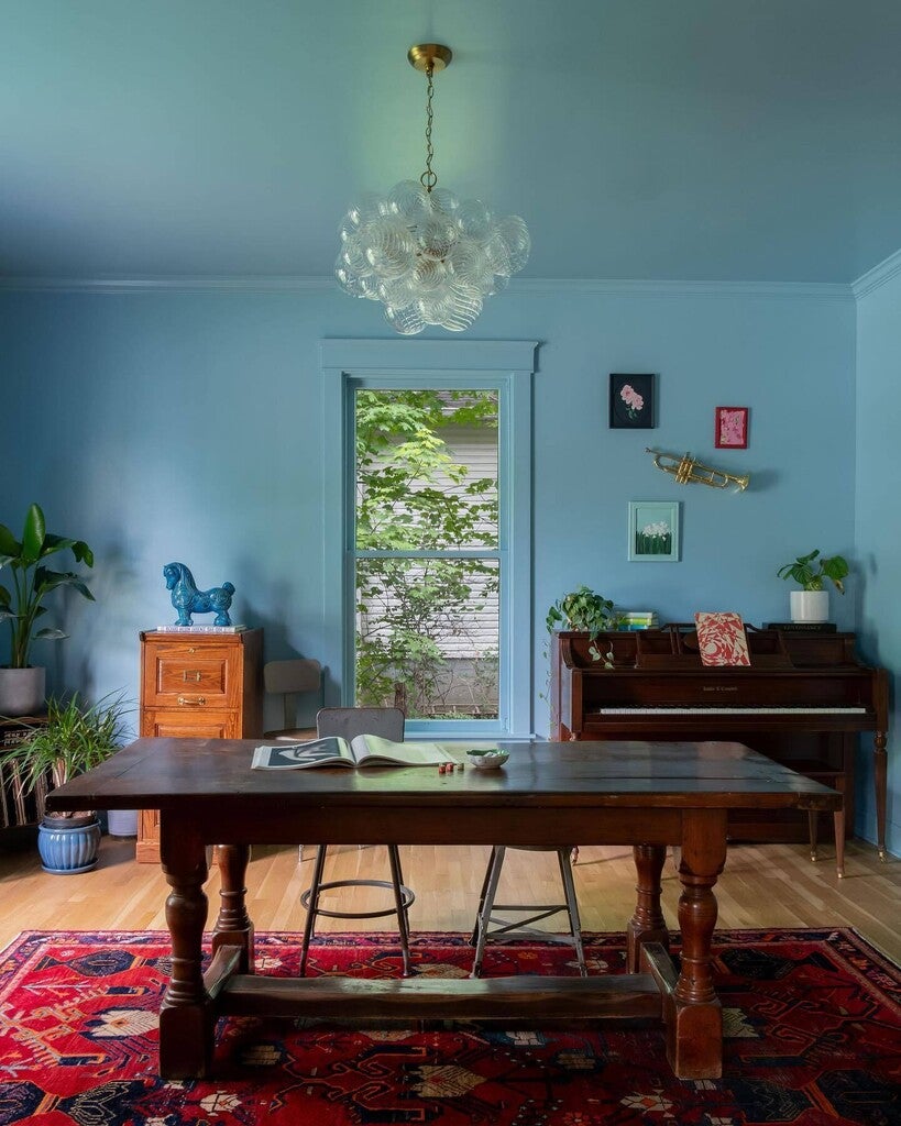 Living room with wooden table, piano, and decorative items against a blue wall.