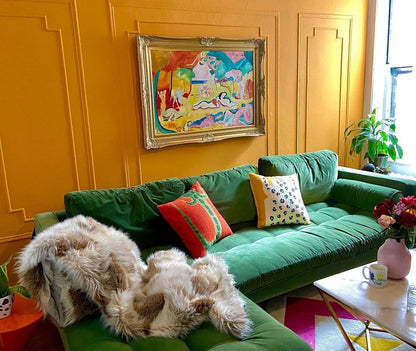 Green sofa with colorful pillows in a room with yellow walls and a painting.