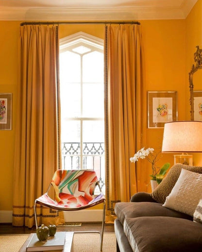 Living room with yellow walls, large window with curtains, and a sofa with a colorful chair.
