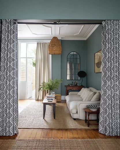 Living room with white sofa, coffee table, and decorative items, featuring patterned curtains.