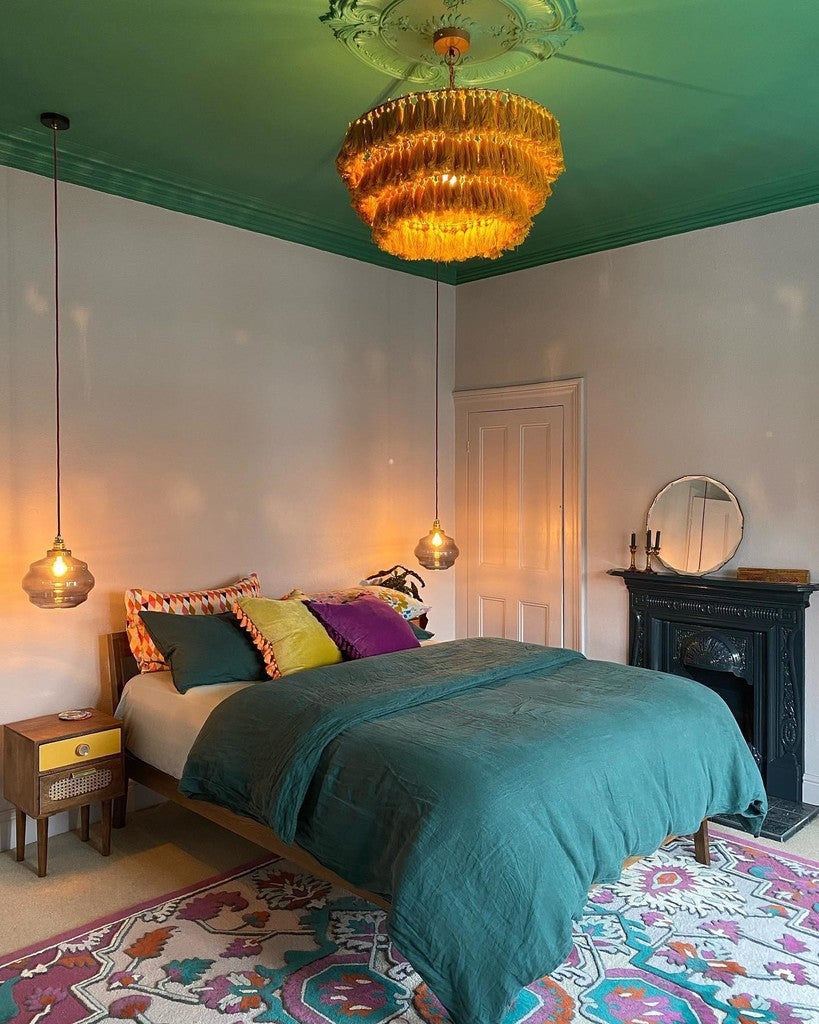 Bedroom with teal ceiling, colorful bedding, and decorative rug.