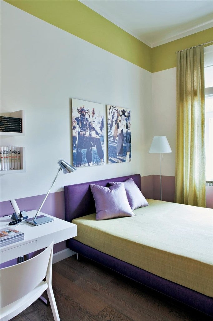Modern bedroom with purple bed, desk, and artwork on a white wall.