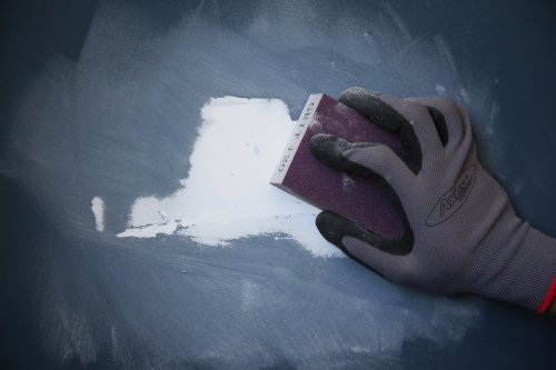 Hand wearing a glove using a sanding block on a dark surface