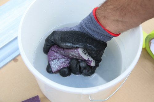 Hand wearing a black glove holding a purple object over a white bucket squeezing it in order for it to be cleaned.