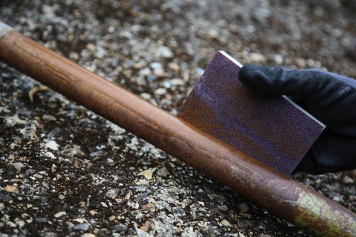 Person wearing a black glove holding a rusty metal rod on a textured surface