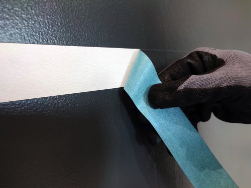 Hand wearing a black glove applying blue tape to a car's edge.