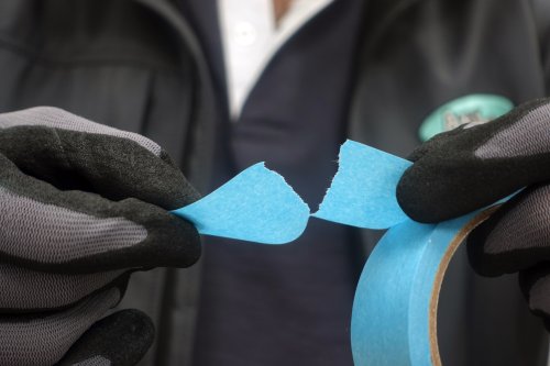 Person wearing black gloves peeling a piece of blue tape