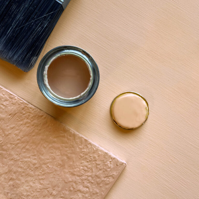 Paint can with brush and lid on a beige surface