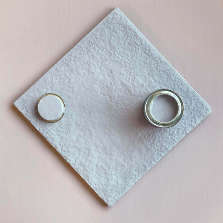 Two curtain rings on a textured white square with a pink background