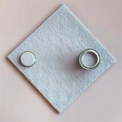 Two curtain rings on a textured white square with a pink background