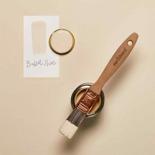 Paint brush with 'earthborn' handle and can of paint on beige background