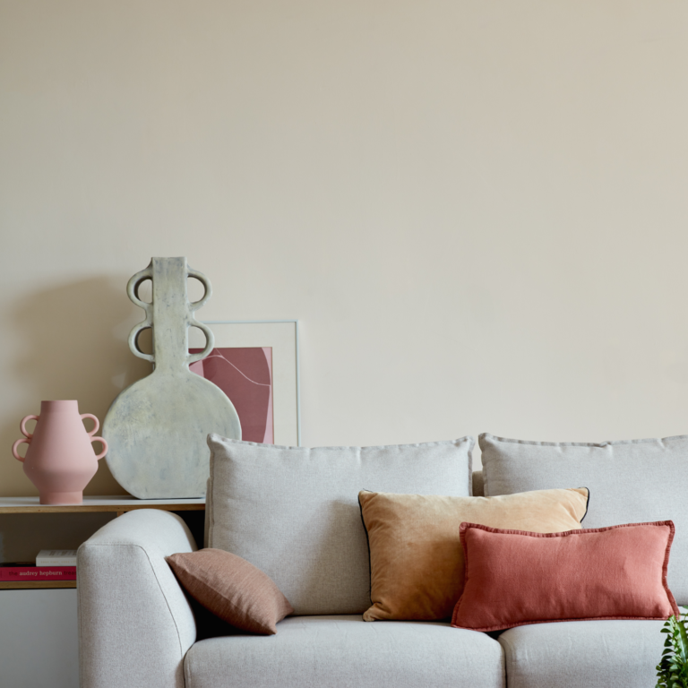 Living room with a gray sofa adorned with colorful cushions, a side table with decorative items, and a plain wall.