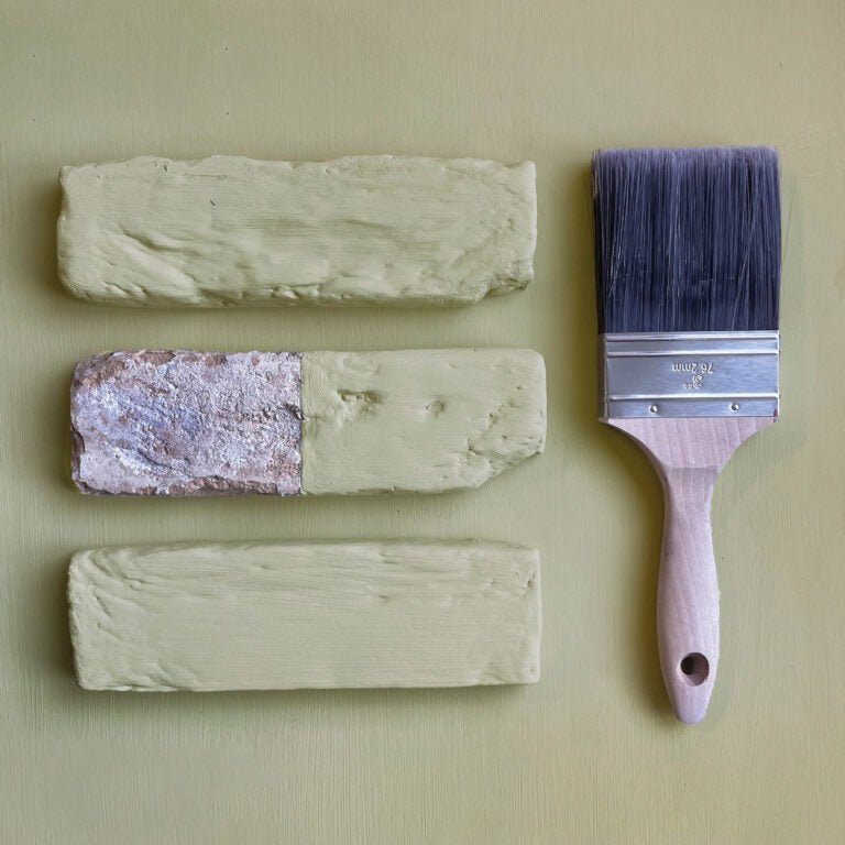 Three swatches of paint and a paintbrush on a beige background