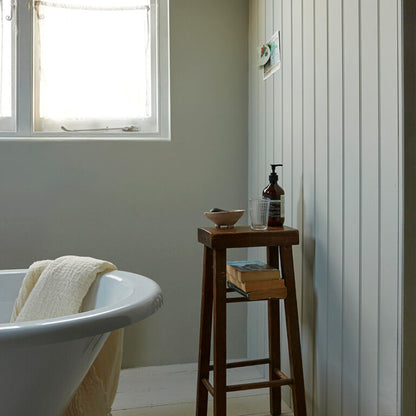 Bathroom with a freestanding bathtub, wooden stool, and various items on a gray wall.