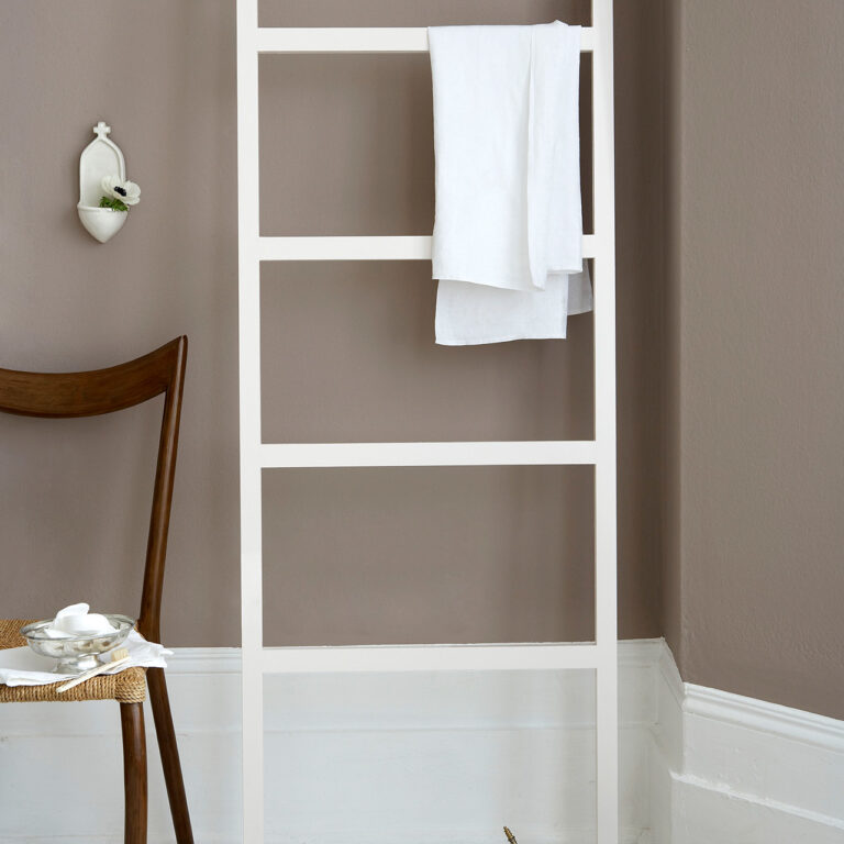 White ladder with towels against a brown wall in a room with a chair and small table.