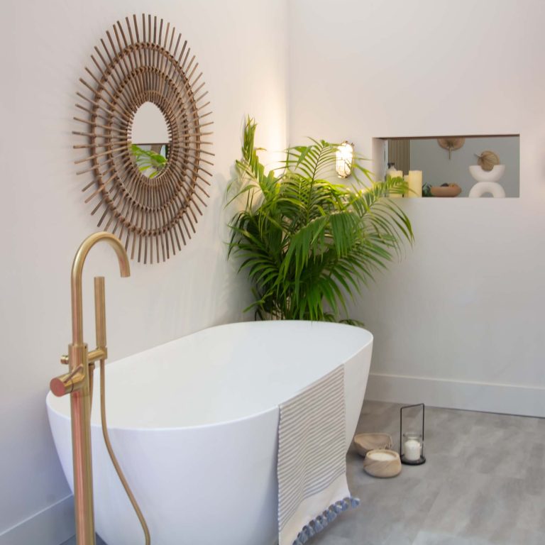 Modern bathroom with freestanding bathtub, gold faucet, and decorative mirror.