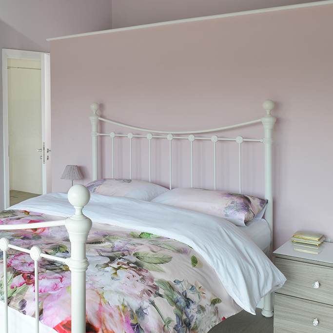 Bedroom with a floral bedspread and white headboard against a pink wall.