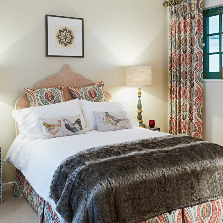 Decorative bedroom with patterned pillows, fur throw, and colorful curtains.