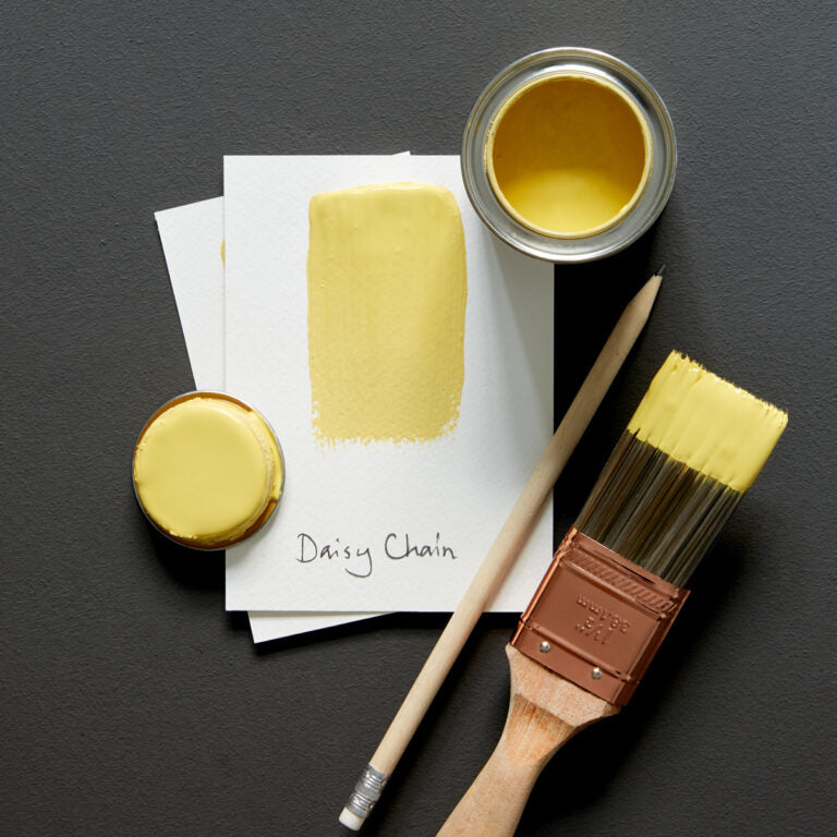Yellow paint can, brush, and color swatch on a dark surface
