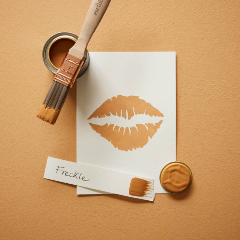 Paint can, brush, and paper with a lipstick print on a beige background