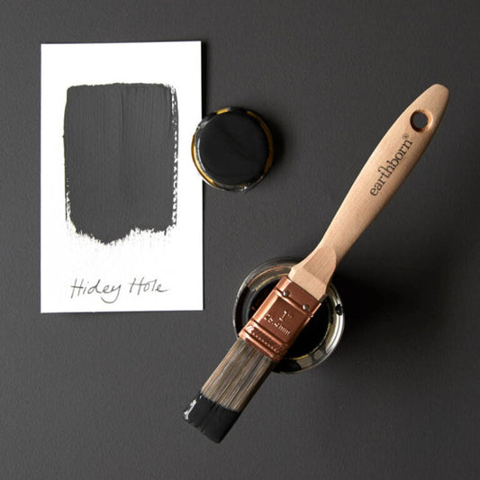 Paintbrush with black paint and color swatch on a dark surface