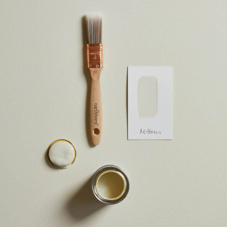 Paintbrush next to a small container of paint and a card on a light background