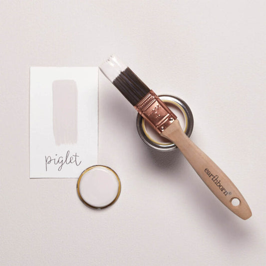 Paintbrush with a container of paint labeled 'Piglet' on a light surface.