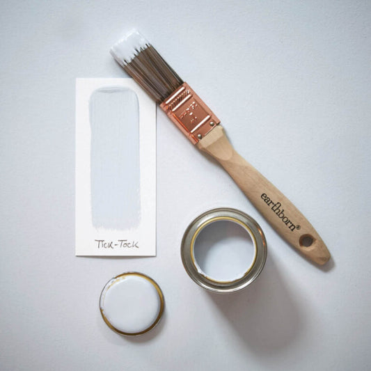 Paint brush and open paint can with 'earthenborn' branding on a light gray background
