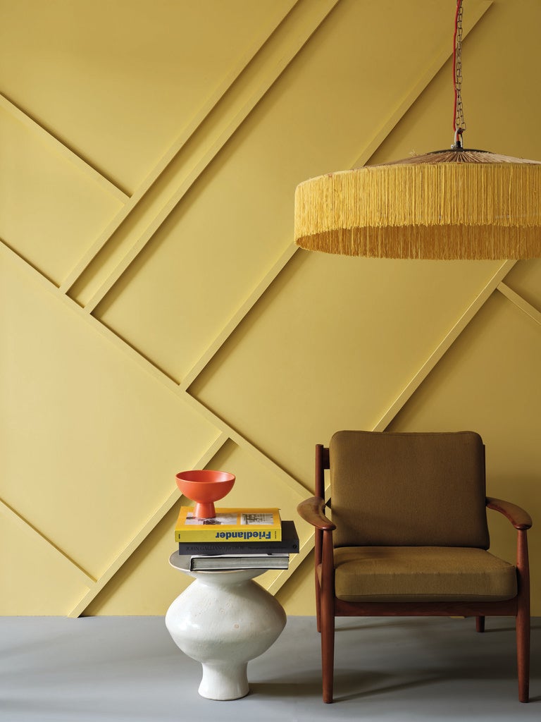 Modern interior with a yellow geometric wall design, brown chair, and small table.