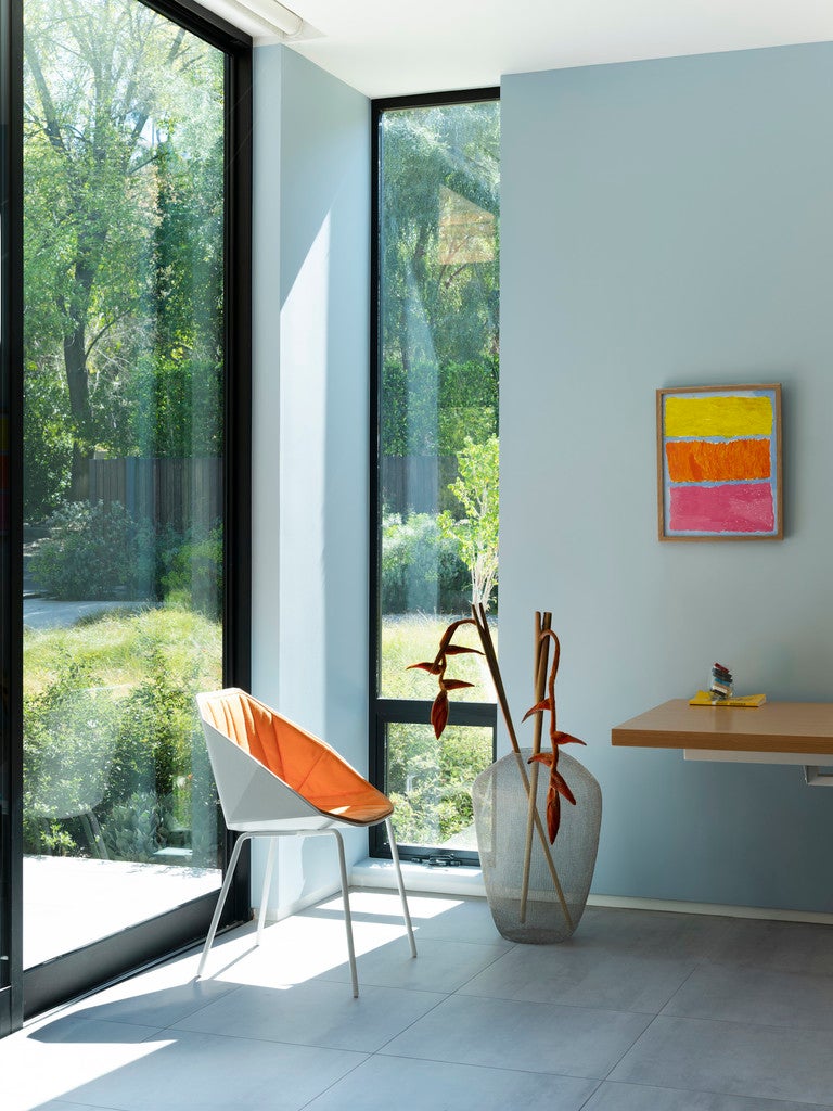 Modern interior with a chair, table, and abstract painting near large windows.