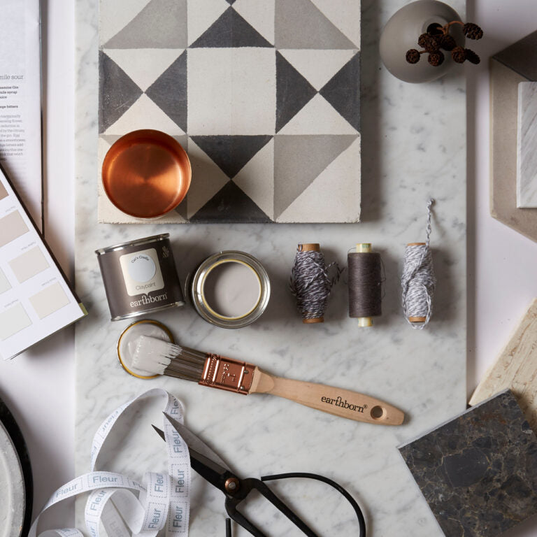 Decorative items including a geometric wall art piece, paint cans, brushes, and measuring tape on a marble surface.