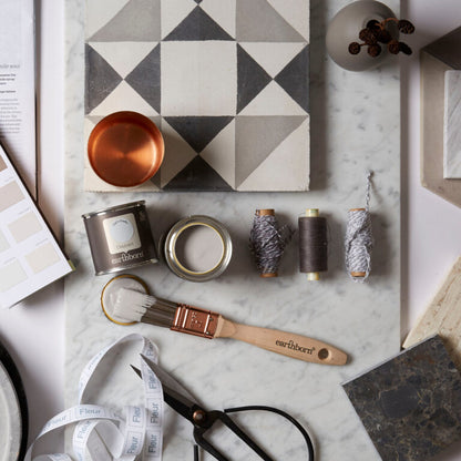 Decorative items including a geometric wall art piece, paint cans, brushes, and measuring tape on a marble surface.