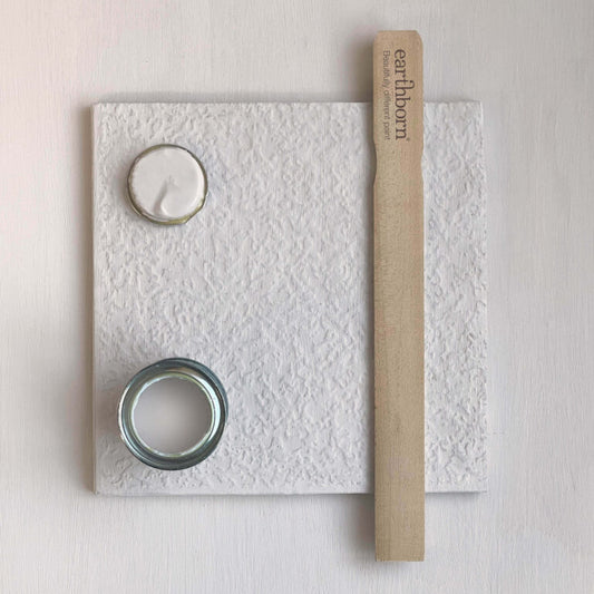 White textured board with two round objects and a wooden stick on a light pink background
