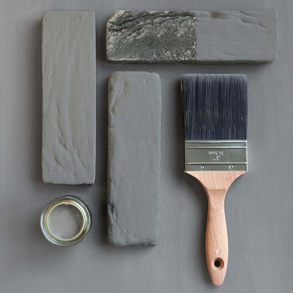 Paint brush with gray paint and stone samples on a gray background