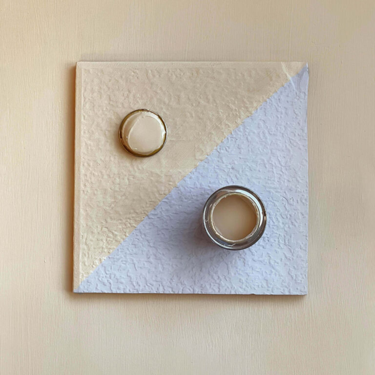 Two round objects on a textured square tile with a beige background