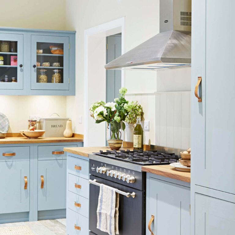 Modern kitchen with light blue cabinets, wooden countertops, and stainless steel appliances.