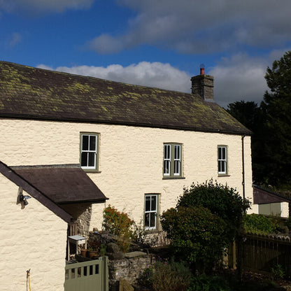 Two-story house with a tiled roof and chimney against a blue sky with clouds.
