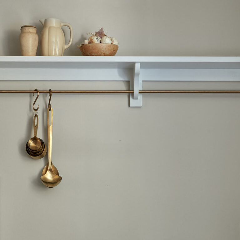 Brass measuring spoons hanging on a hook with a shelf and decorative items in the background.