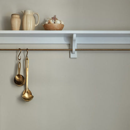 Brass measuring spoons hanging on a hook with a shelf and decorative items in the background.