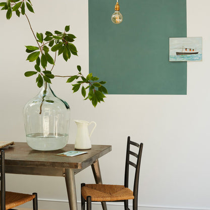 Dining area with a wooden table, chairs, a vase with greenery, and a painting on the wall.