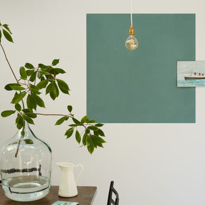 Modern interior with a green wall, light bulb, plant, and pitcher.