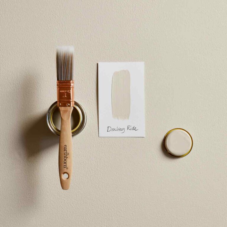 Paintbrush with a container of paint and a stencil on a beige surface