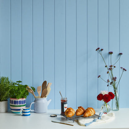Table with croissants, jam, and a vase of flowers against a blue paneled wall.